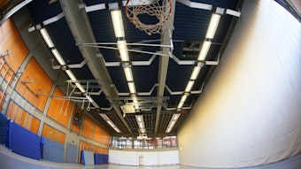 Eine leere Sporthalle im Schulzentrum Oberpleis. Oben ist ein Basketballkorb zu sehen, an einer Seitenwand lehnen blaue Sportmatten.