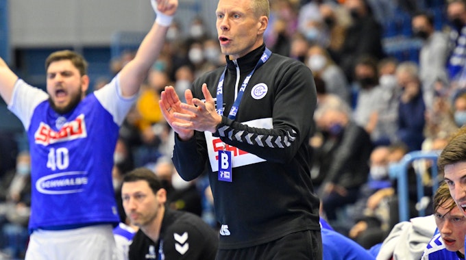 VfL-Trainer Gudjon Valur Sigurdsson steht am Rand des Handballfeldes und gestikuliert mit den Händen. Im Hintergrund jubelt VfL-Kreisläufer Jonas Stüber.