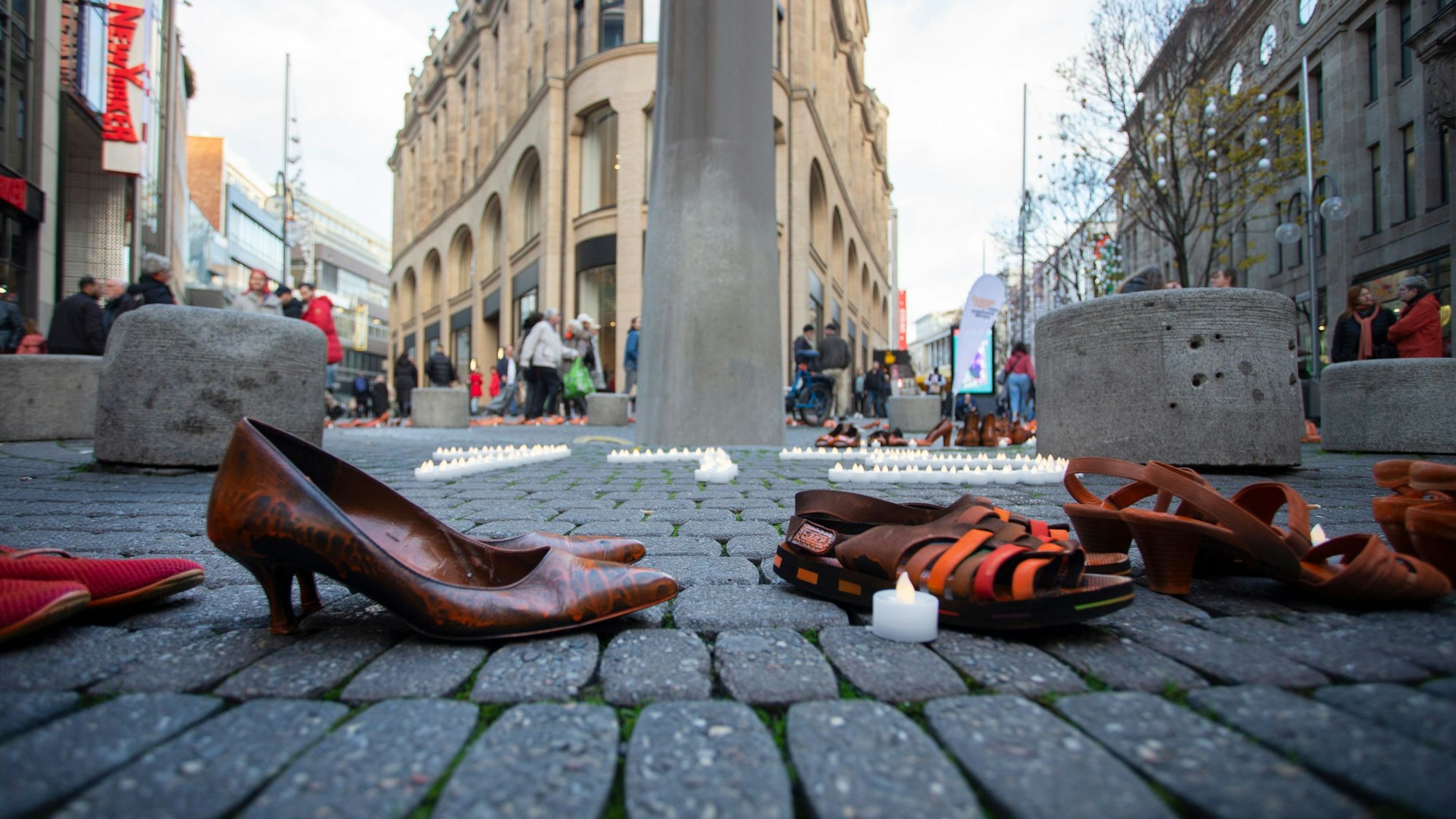 Schuhe von Frauen stehen auf der Kölner Schildergasse, umringt von Teelichten.