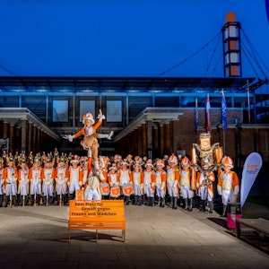Die KKG Nippeser Bürgerwehr 1903 e.V. steht mit oranger Kleidung vor dem Rhein-Energie-Stadion und setzt damit ein Zeichen gegen Gewalt an Frauen.