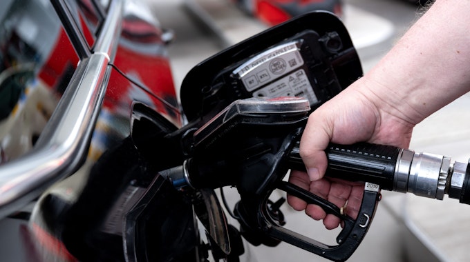 Ein Mann hält eine Zapfpistole an einer Tankstelle in der Hand und betankt sein Auto.