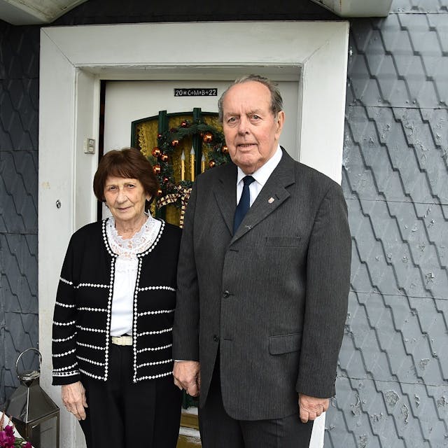 Zu sehen sind eine Frau und ein Mann, beide schick gekleidet, vor der Haustür ihres Wohnhauses in Bergneustadt.