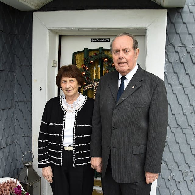 Zu sehen sind eine Frau und ein Mann, beide schick gekleidet, vor der Haustür ihres Wohnhauses in Bergneustadt.