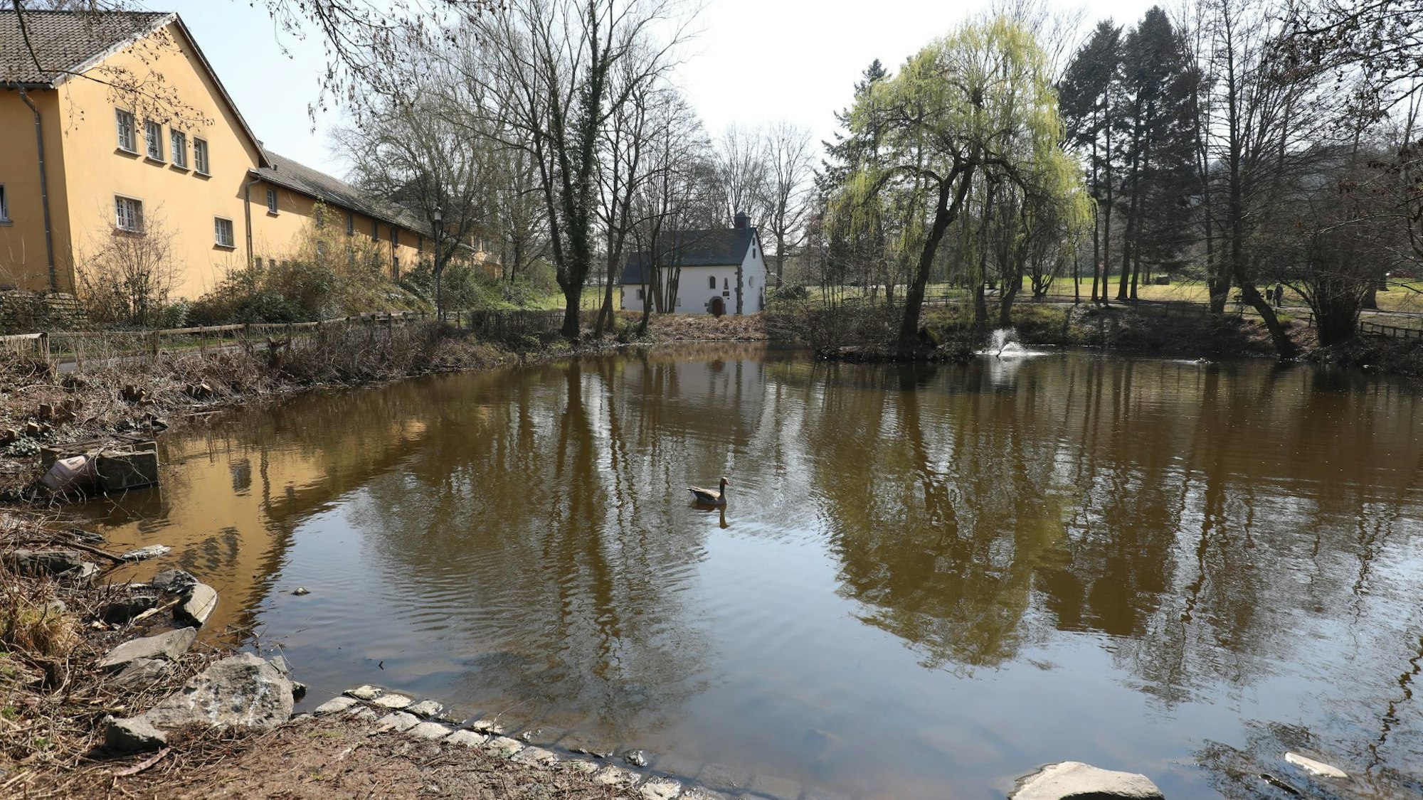 Ein Teich mit relativ niedrigem Wasserstand, im Hintergrund steht eine kleine Kapelle.