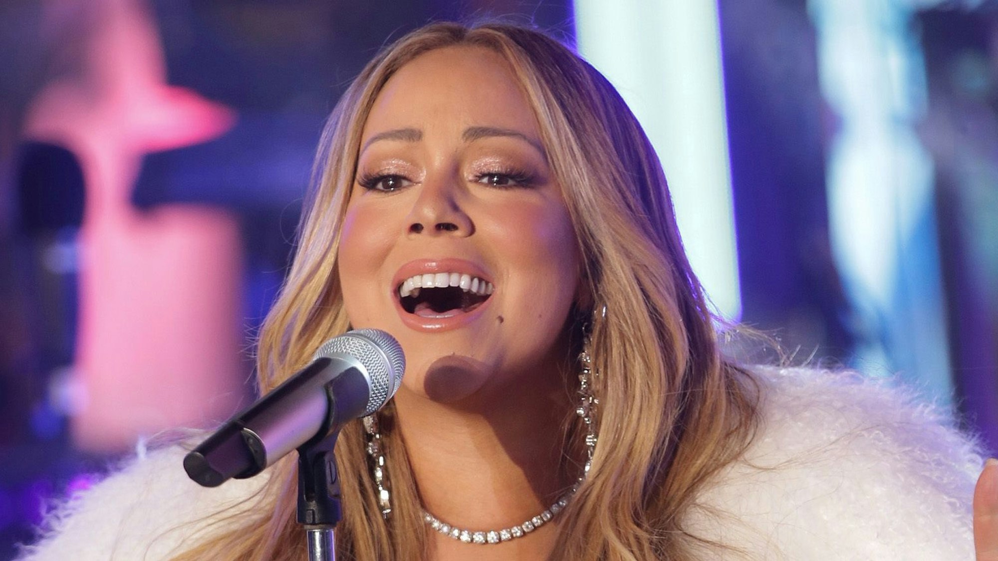 Mariah Carey tritt bei der Silvesterfeier 2018 auf dem Times Square auf. Sie singt in ein Mikrofon und trägt einen weißen Kunstpelz.