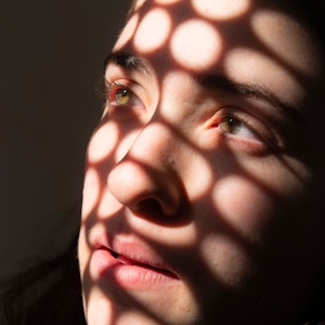 Porträt eines Mädchens, das traurig in ein Licht schaut, das runde Schatten auf sein Gesicht wirft.