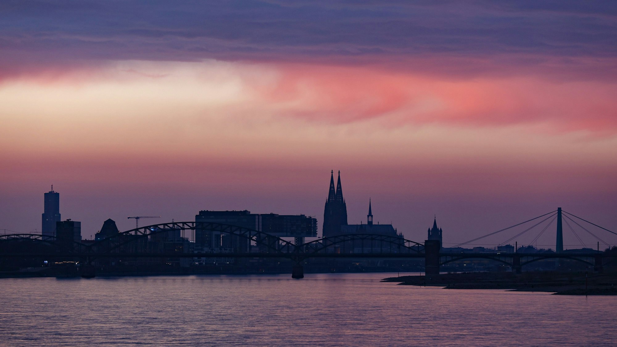 Das Bild zeigt die Skyline Kölns mit rötlichem Sonnenuntergang.