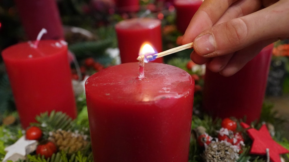 Eine Frau zündet mit einem Streichholz eine Kerze im Adventskranz an.