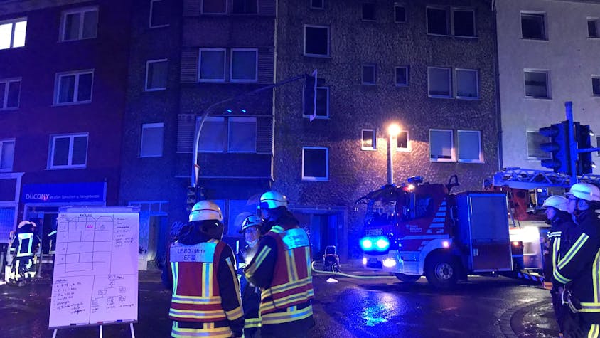Autos und Einsatzkräfte der Feuerwehr stehen vor einem Mehrfamilienhaus in Bochum. Bei einem Brand ist eine Person ums Leben gekommen.
