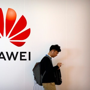 Ein Mann tippt auf seinem Smartphone, während er auf der Fachmesse PT Expo in der Nähe einer Werbetafel für die chinesische Technologiefirma Huawei steht.