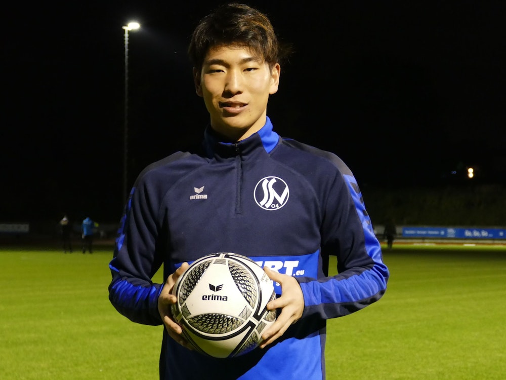 Kaito Asano vom Siegburger SV 04 steht mit einem Fußball in der Hand am Spielfeld.