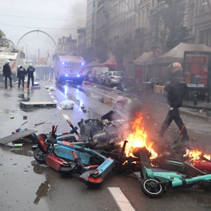 Polizisten gehen an Brand geratenem Müll und Leih-E-Scootern, die mitten auf der Straße in Brüssel liegen, vorbei.