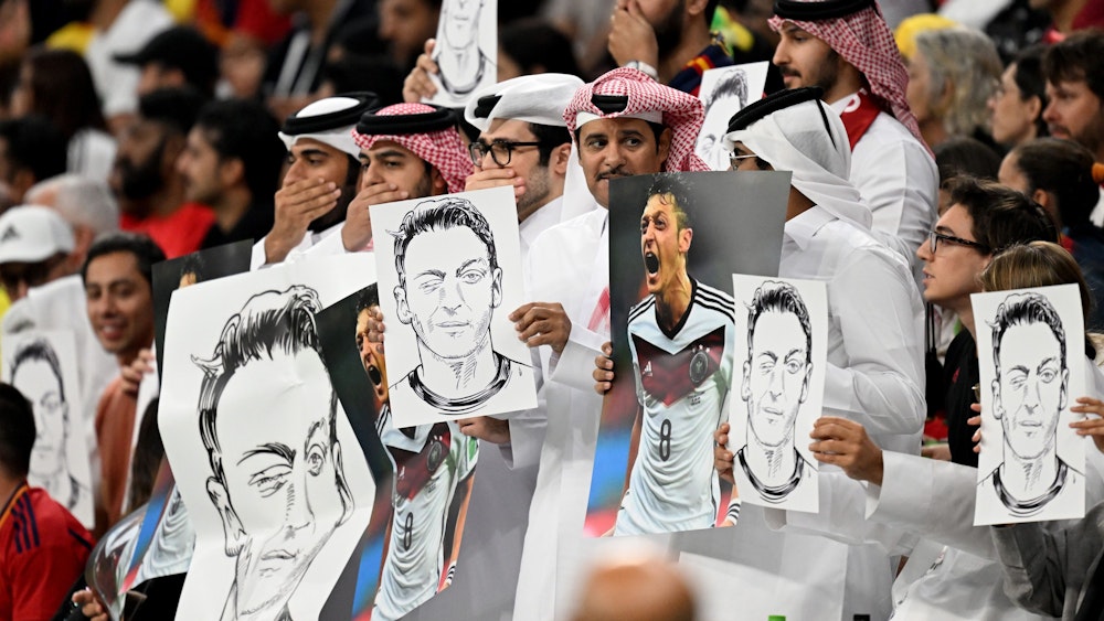 Zuschauer im Al-Bait Stadion halten Bilder von Deutschlands ehemaligem Nationalspieler Mesut Özil in die Höhe.