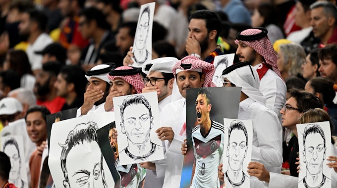 Zuschauer im Al-Bait Stadion halten Bilder von Deutschlands ehemaligem Nationalspieler Mesut Özil in die Höhe.