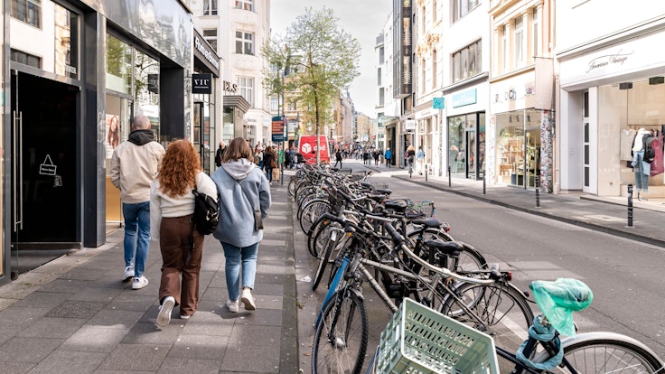 Menschen spazieren über die Ehrenstraße in Köln, daneben sind dutzende Fahrräder abgestellt.