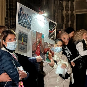 Hunderte Kölner singen „Another Love“ auf der Domplatte. Demonstrantinnen, einige mit Schutzmaske, halten Plakate hoch.