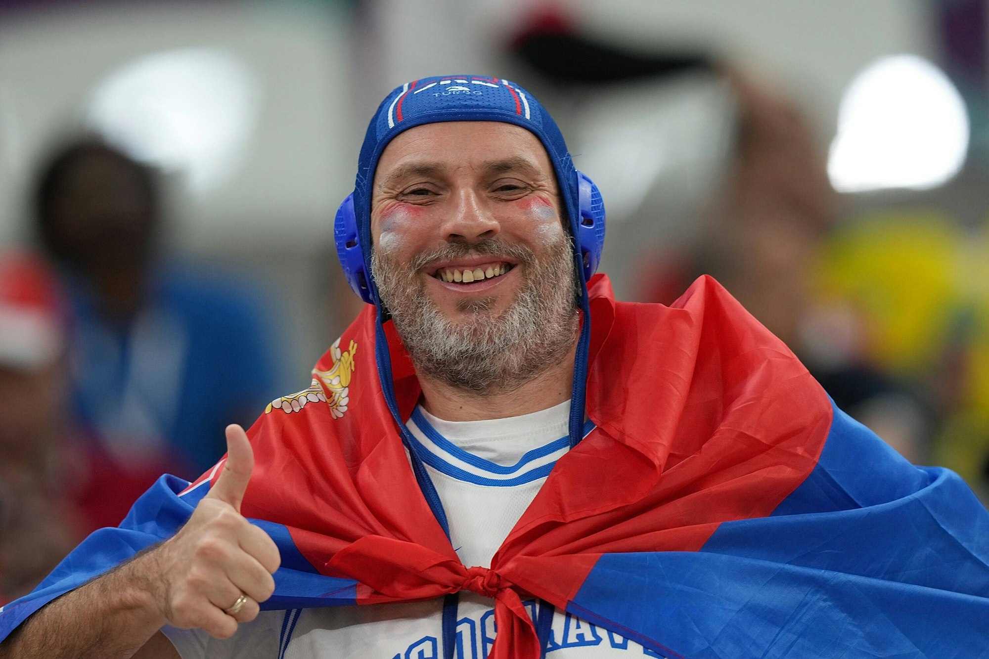 Ein serbischer Fan trägt einen Wasserball-Kopfschutz und zeigt dabei einen Daumen hoch in die Kamera.