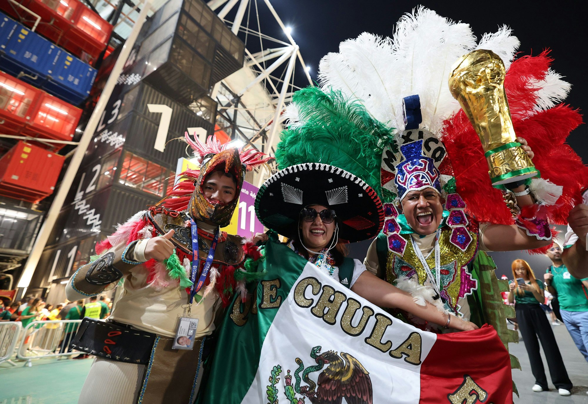 Drei Fans der mexikanischen Nationalmannschaft stehen in ihren bunten Kostümen vor einem Stadion in Katar.