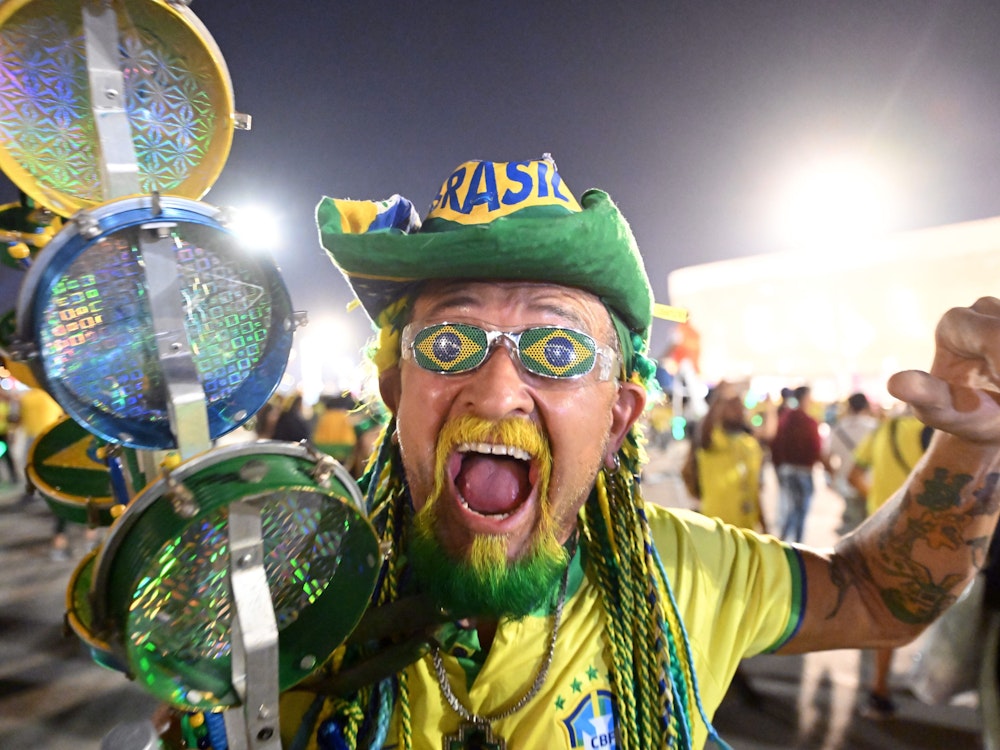 Ein Brasilianer mit gelb-grünem Bart und Haar macht eine jubelnde Geste auf der Straße.