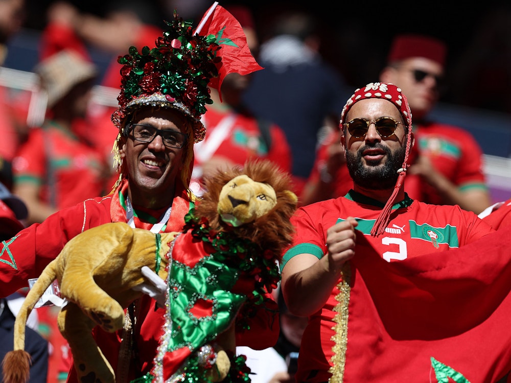 Zwei Fans der marokkanischen Nationalmannschaft stehen auf der Tribüne und halten ein Löwen-Plüschtier vor sich.
