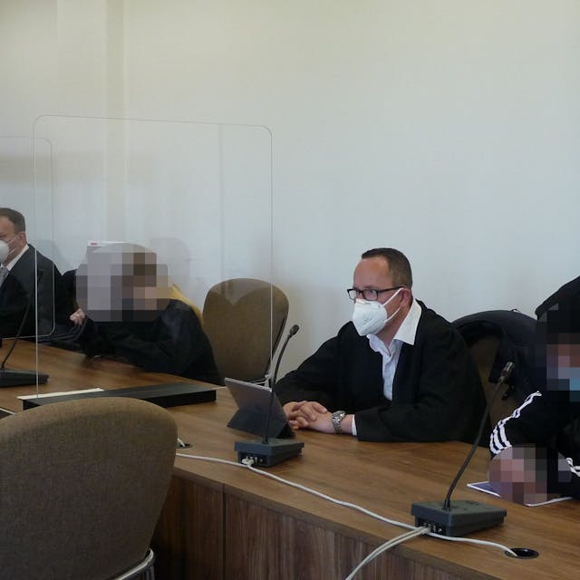 Eine Frau und ein Mann mit gepixelten Gesichtern sowie zwei Männer in Anwaltsrobe sitzen am Tisch einer Anklagebank im Kölner Landgericht.
