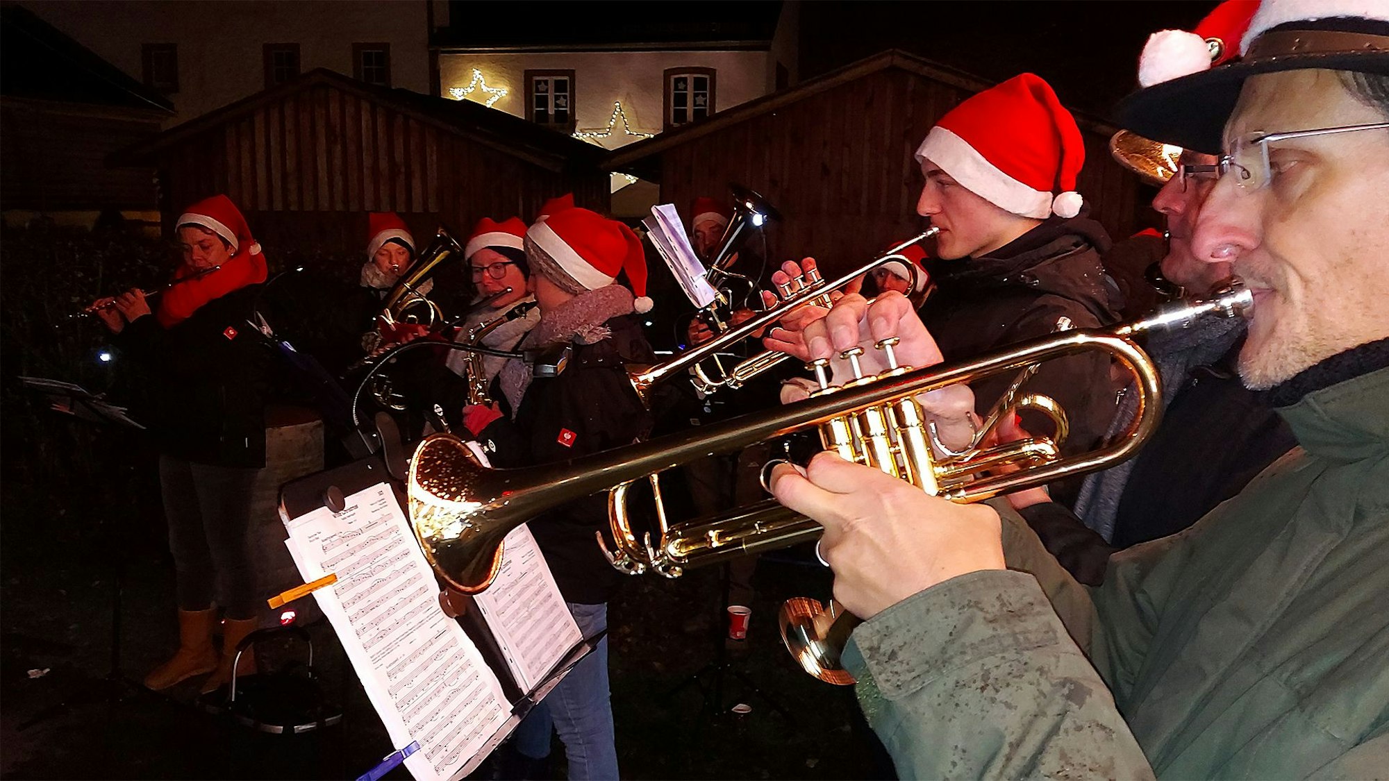 Die Mitglieder des Musikvereins Hecken haben rote Weihnachtsmützen aufgesetzt und spielen auf dem Weihnachtsmarkt in Reifferscheid, im Vordergrund zwei Trompeter.