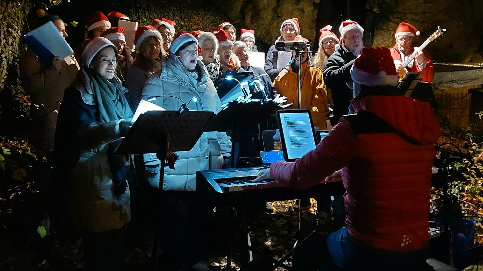 Die Mitglieder des Chors Kakus Vocale haben rote Weihnachtsmützen angezogen und singen Weihnachtslieder, begleitet von Uli Schneider am Keyboard.