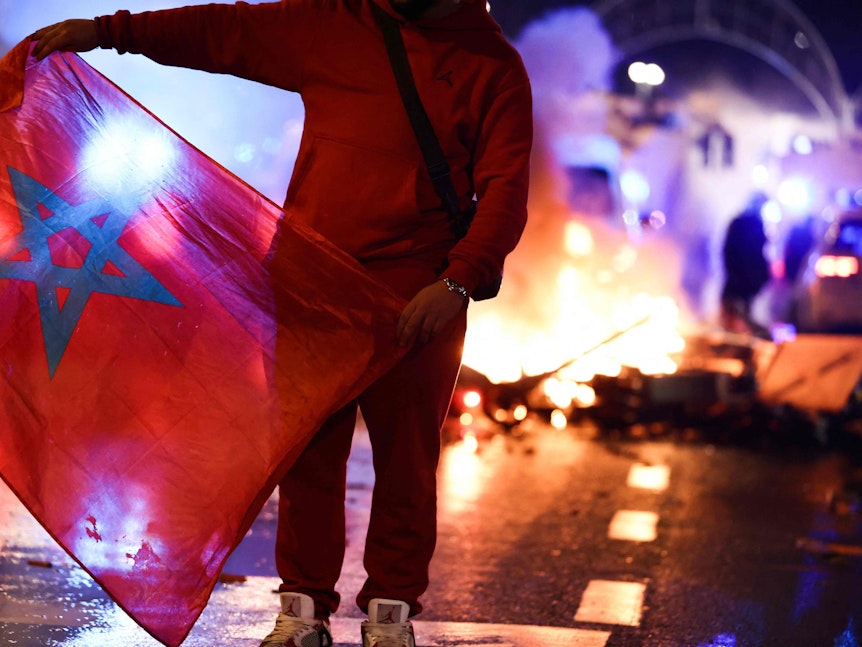 Ein Fan steht am Sonntagabend (27. November 2022) auf einer Straße der belgischen Hauptstadt. Im Hintergrund brennt eine Barrikade.