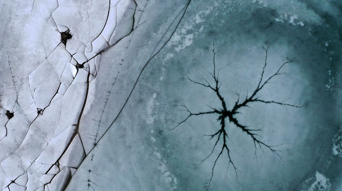 Bayern: Ein sternförmiger Riss ist auf der Eisfläche des Forggensees neben am Ufer liegenden gebrochenen Eisplatten zu sehen.