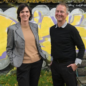 Sigrid Schule und André Eigenbrod, die neuen Leiter der Kreaschule in Bergisch Gladbach, stehen vor einer mit gelb-lilanen Graffitis verzierten Wand.