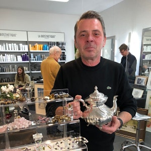 Friseurmeister Ralph Schwalbach steht in seinem Salon an der Luxemburger Straße und hält eine Kanne aus Silber in der Hand.