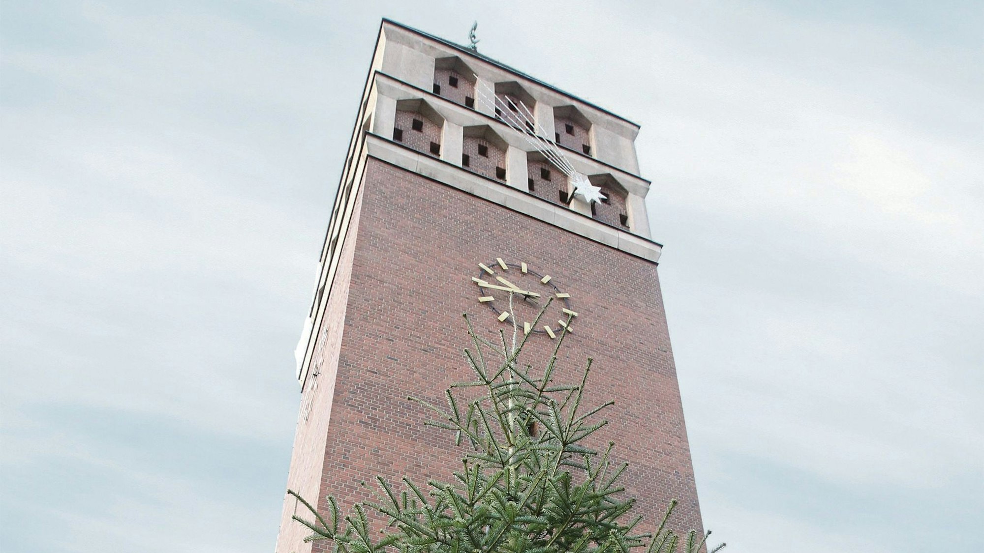 Der Kirchturm der Pfarrkirche St. Hippolytus in Troisdorf mit einem Weihnachtsbaum davor.