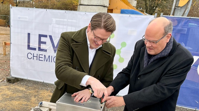Marius Mühlenberg, CEO von Levaco, schraubt mit Finanzchef Jens Becker an der Metallkiste, die in den Grundstein gelegt wird.