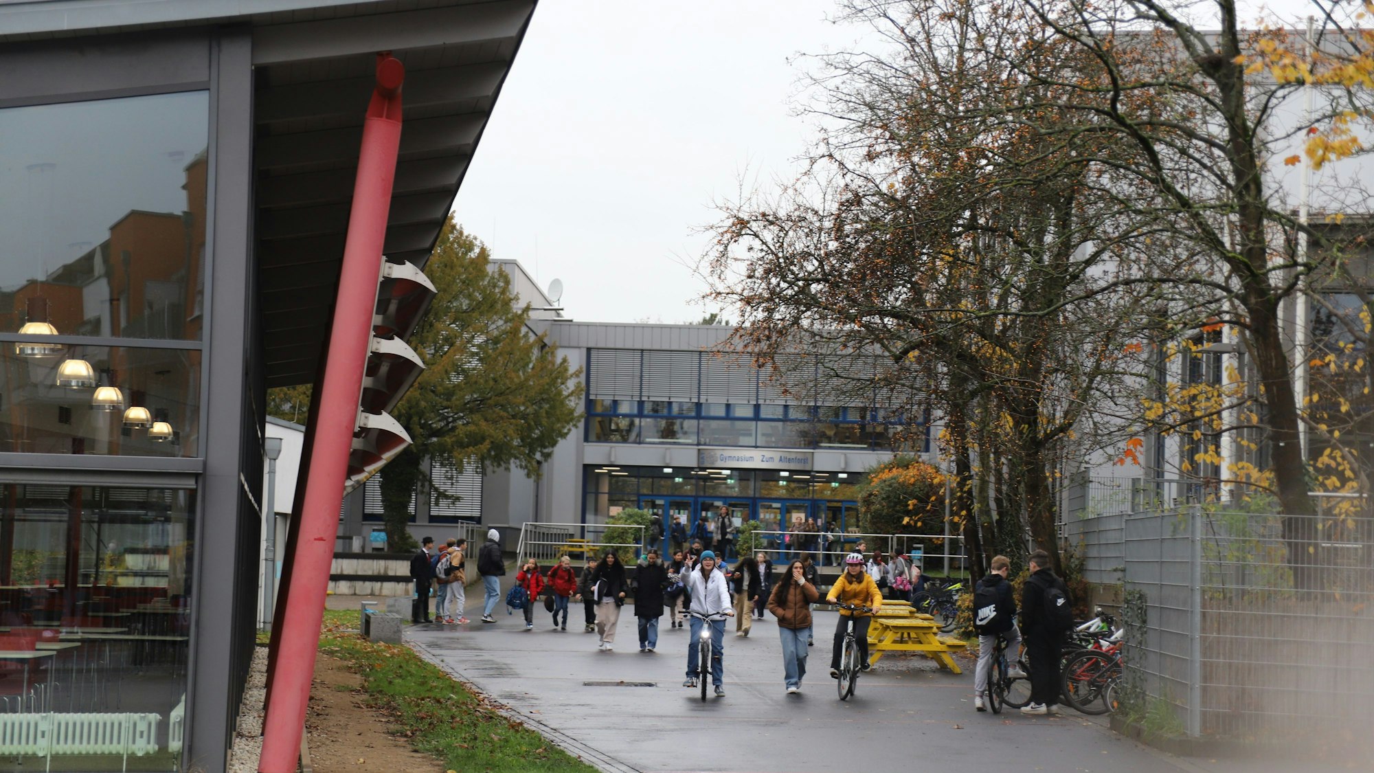 Schüler und Schülerinnen sind zu Fuß und mit dem Rad vor dem Gebäude des Gymnasiums Zum Altenforst in Troisdorf unterwegs.