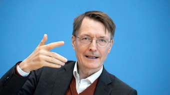Gesundheitsminister Karl Lauterbach im Anzug vor einem blauen Hintergrund.