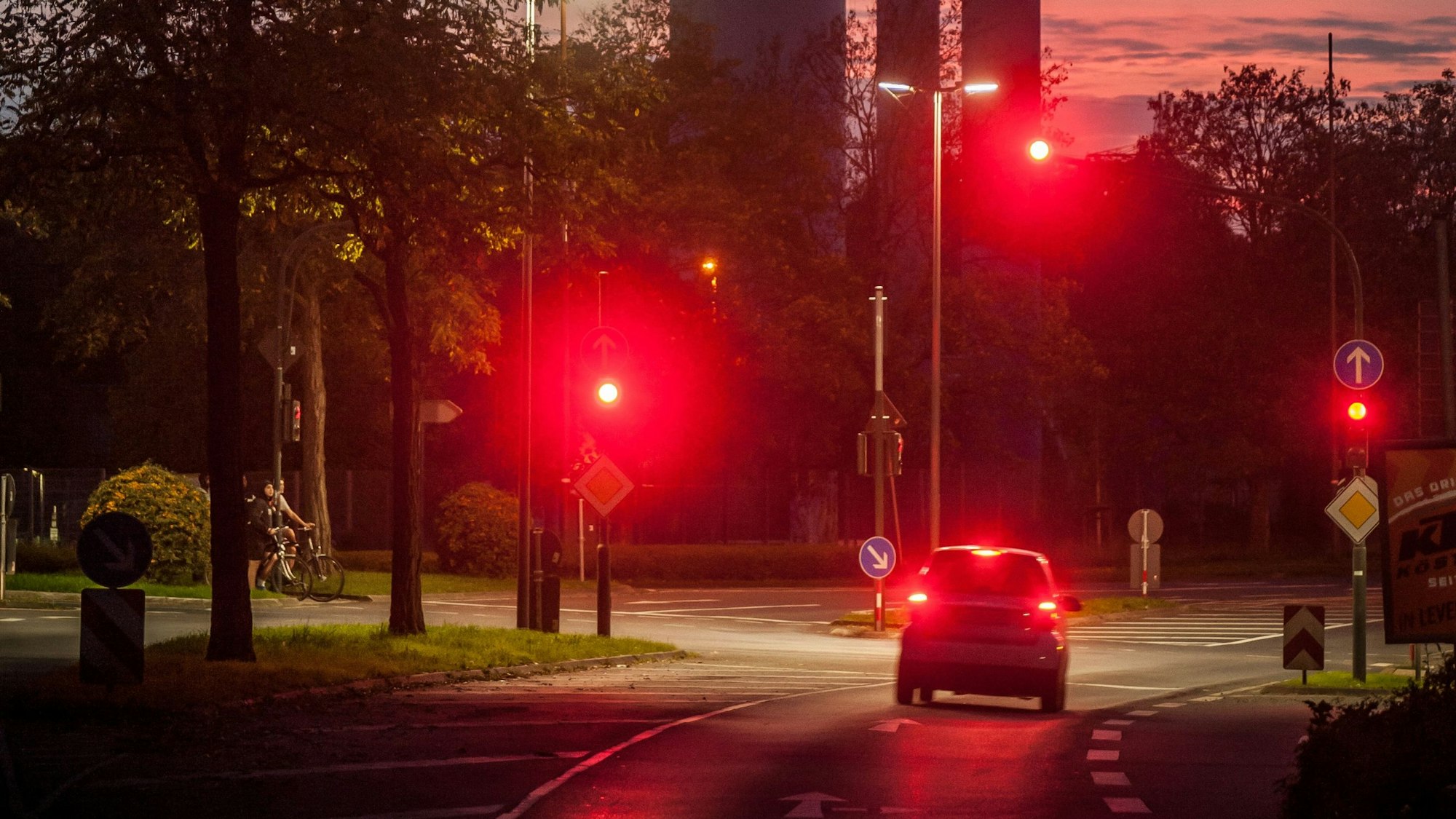 Im Abendlicht steht ein Kleinwagen mit rot leuchtenden Bremslichtern an einer roten Ampel. Dahinter ist der EVL-Turm zu sehen.