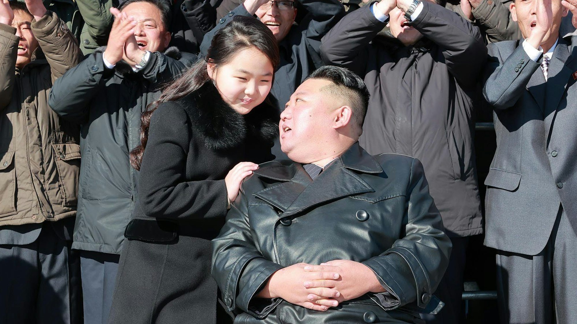 Kim Jong Un und seine Tochter unterhalten sich, im Hintergrund feiern nordkoreanische Bürger das Duo.