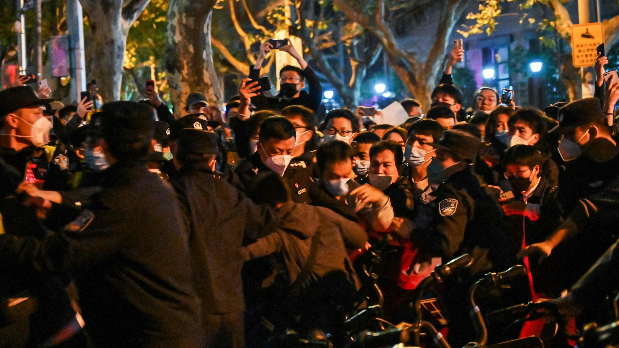 Menschen mit Masken und Polizisten drängen sich bei einem Protest in Shanghai gegen die strenge Corona-Politik Chinas.