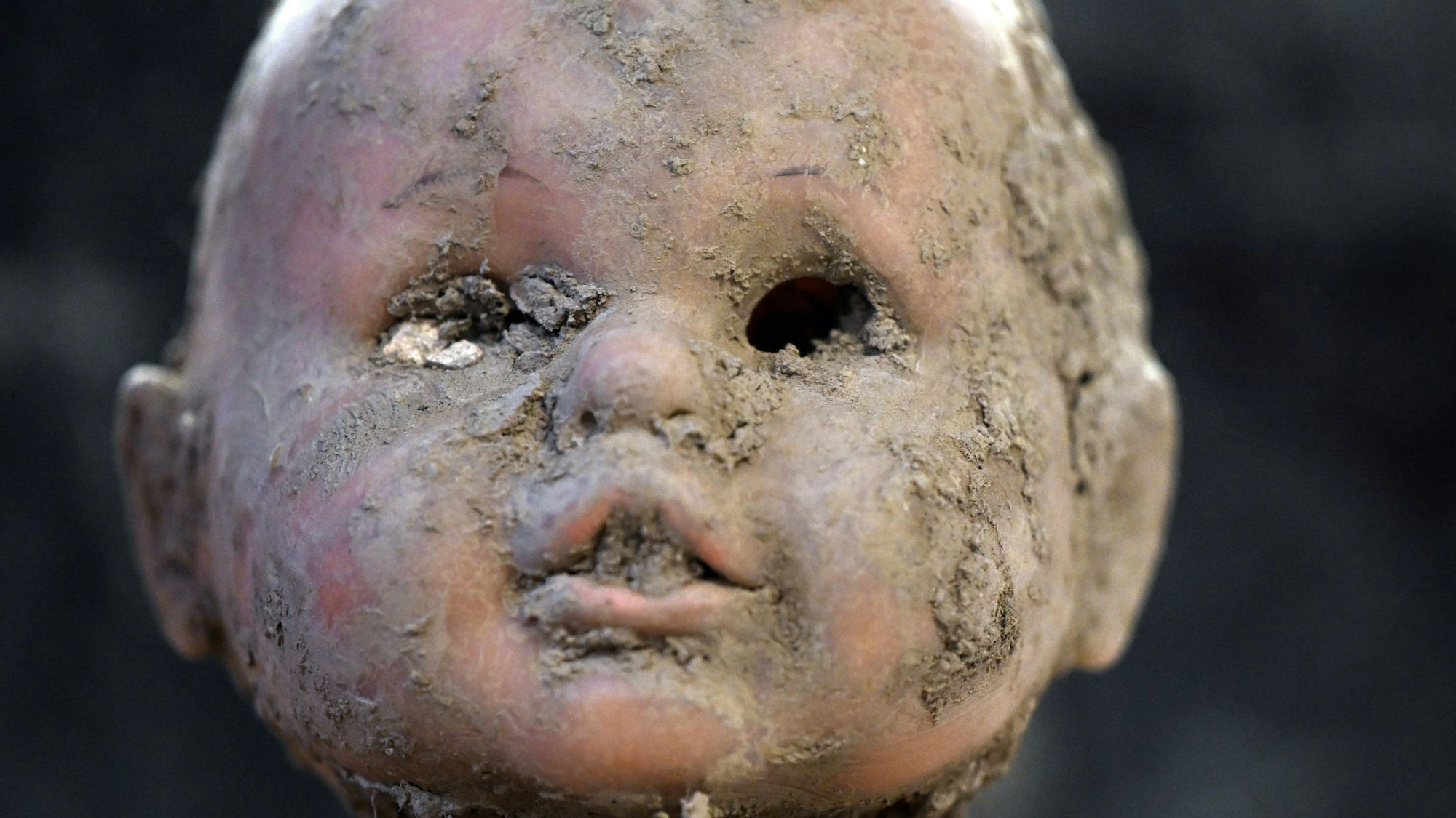 Der Kopf einer Puppe ist verschlammt, im Mund steckt Dreck, die Augen fehlen.