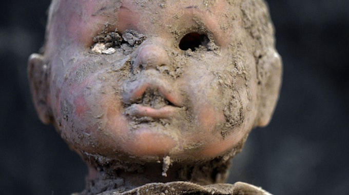 Der Kopf einer Puppe ist verschlammt, im Mund steckt Dreck, die Augen fehlen.