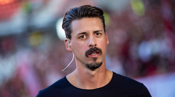 Der ehemalige deutsche Fußball-Nationalspieler Sandro Wagner trägt ein Headset und steht vor einem Spiel im Stadion. Er blickt in die Kamera.