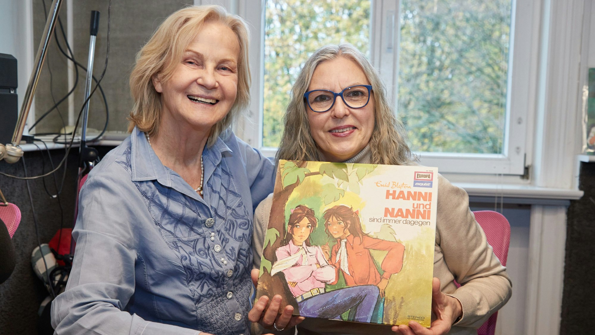 Heikedine Körting (l), Produzentin, und Manuela Dahm, Sprecherin, sitzen während eines Fototermins zu 50 Jahre „Hanni und Nanni“-Hörspiele im Tonstudio am Rothenbaum. Sie halten die erste Platte „Hanni und Nanni sind immer dagegen“ in den Händen