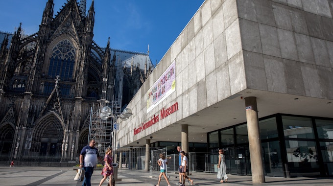 Menschen laufen über die Domplatte am Dom und dem Römisch-Germanischen Museum vorbei