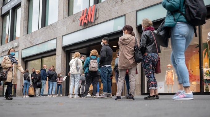 Kundinnen und Kunden stehen in einer Schlange vor einer H&M-Filiale.