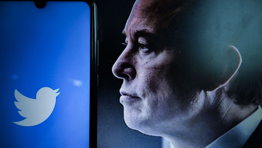 Ein Blick auf das Logo des amerikanischen Social-Networking-Unternehmens Twitter auf einem Smartphone-Bildschirm neben einem Porträt des Unternehmers Elon Musk.
