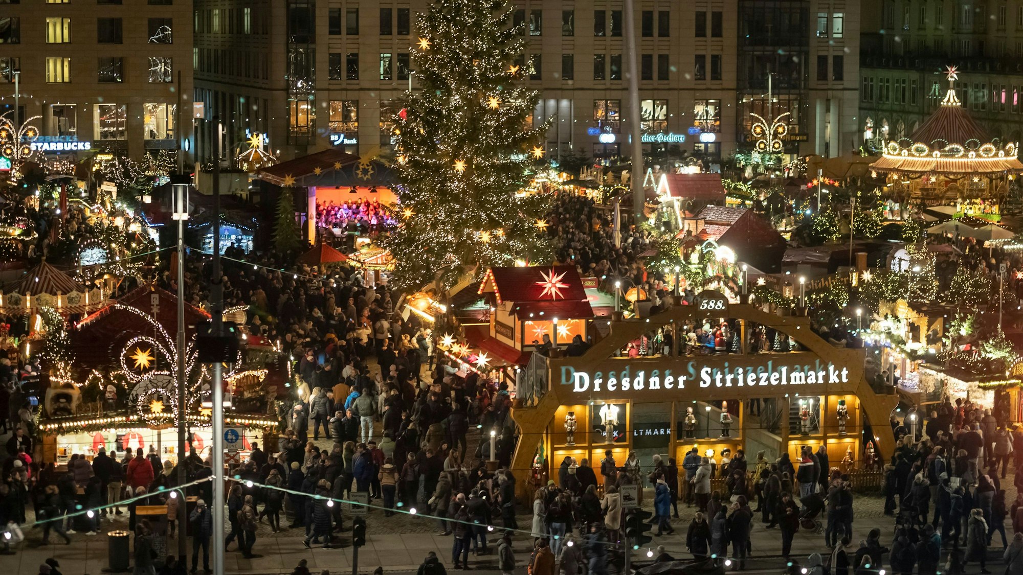 Besucher laufen zwischen festlich dekorierten Ständen und Weihnachtsbäumen über den Weihnachtsmarkt in Dresden.