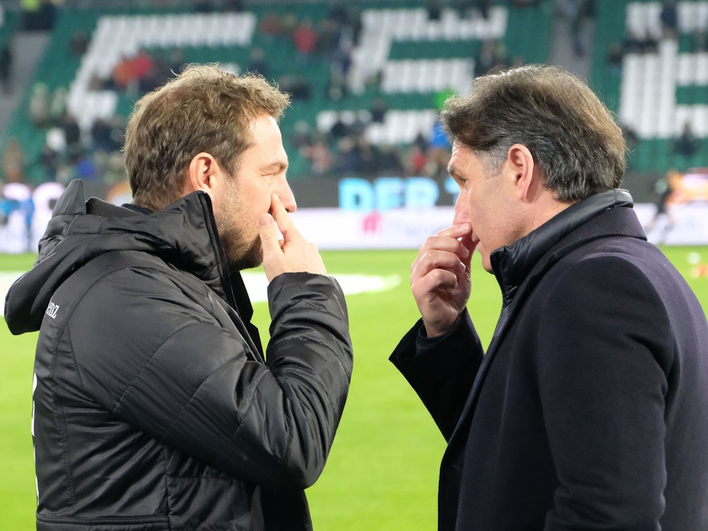 Markus Weinzierl (l) und Bruno Labbadia sprechen vor einem Spiel miteinander und fassen sich gleichzeitig ins Gesicht.
