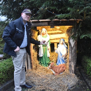 Ein Mann steht vor einer Krippe mit dargestelltem Josef, Maria und einer Kuh und hält die abgeschlagene Hand einer der Figuren. Die Jesus-Figur und ein Esel fehlen.