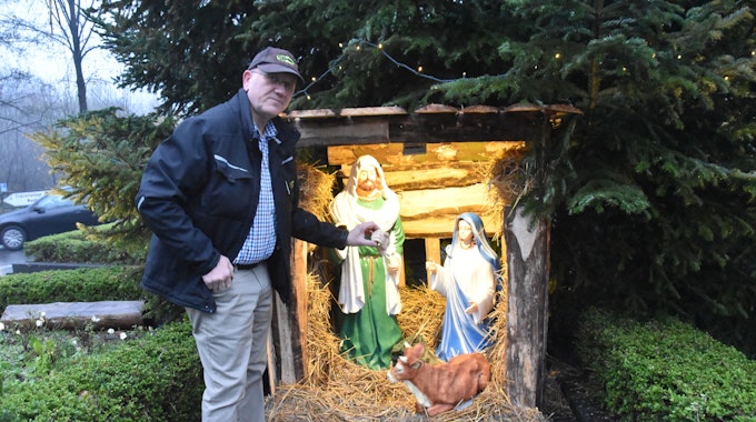 Ein Mann steht vor einer Krippe mit dargestelltem Josef, Maria und einer Kuh und hält die abgeschlagene Hand einer der Figuren. Die Jesus-Figur und ein Esel fehlen.