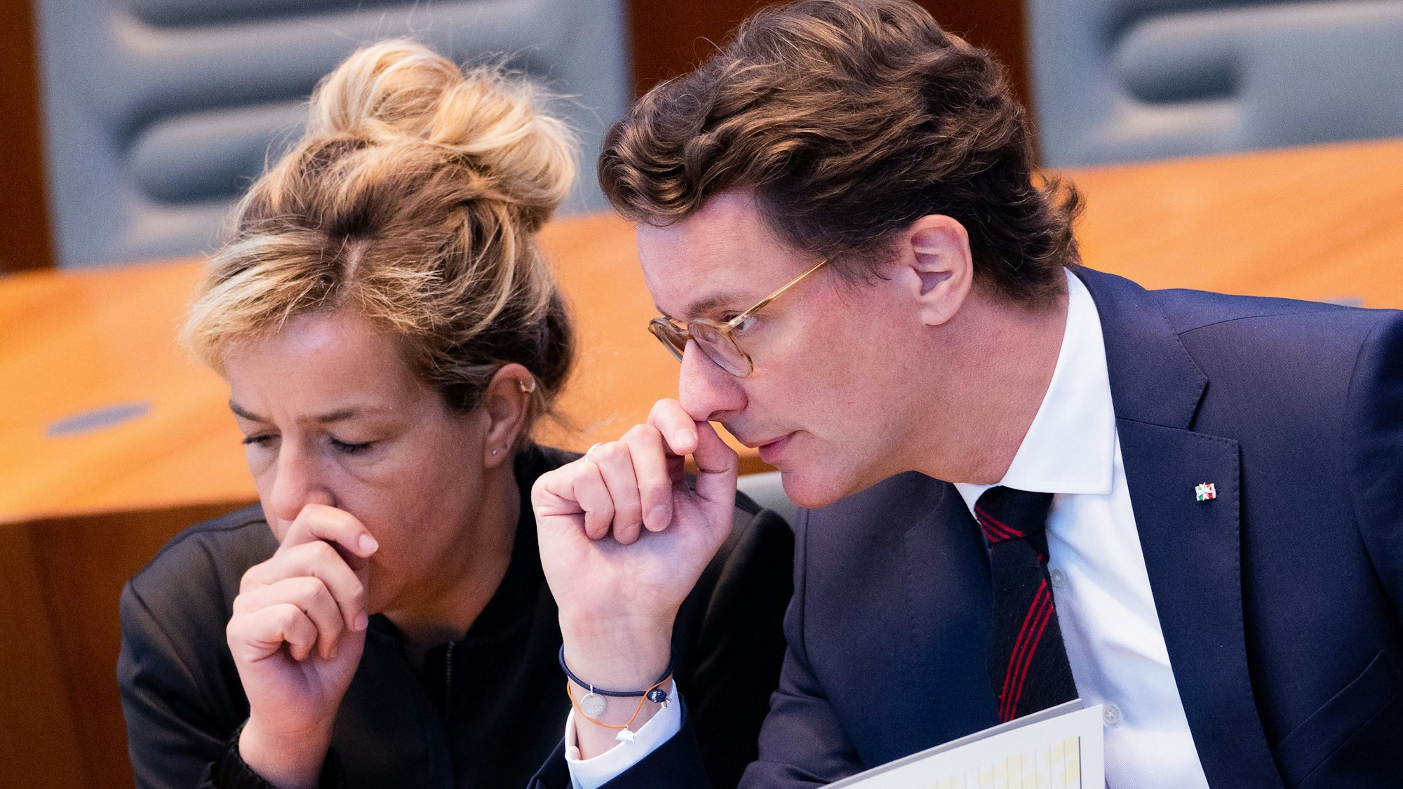 Die NRW-Politiker Mona Neubaur und Hendrik Wüst sitzen im Landtag, sie gucken besorgt, beide halten sich die Hände vor das Gesicht.